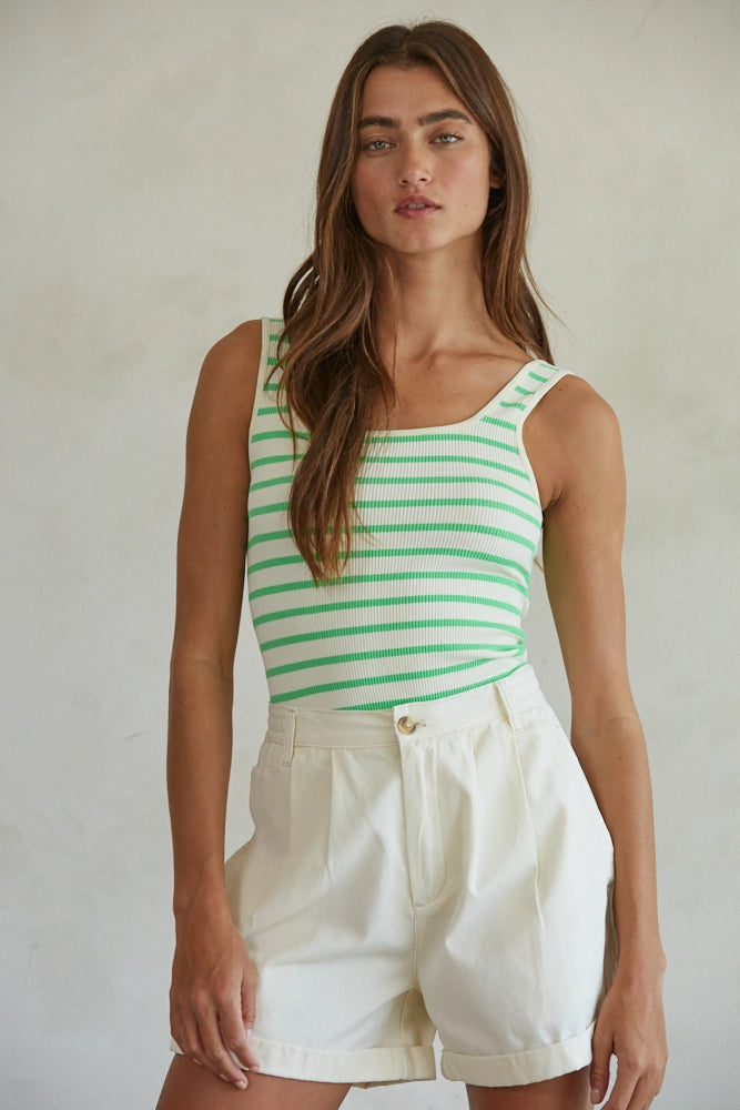 Woman wearing a green and white striped tank top and white shorts against a plain background