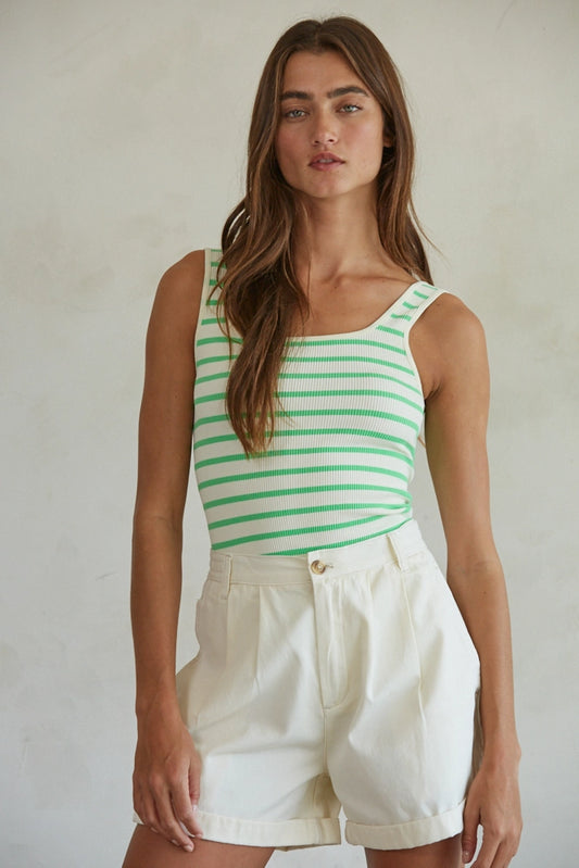Woman wearing a green and white striped tank top and white shorts against a plain background
